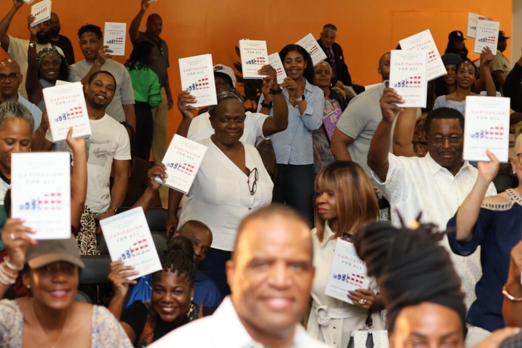 Audience members hold up copies of Capitalism for All