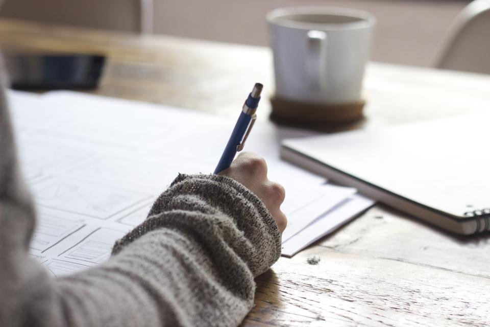 A hand writing in a notebook at a desk