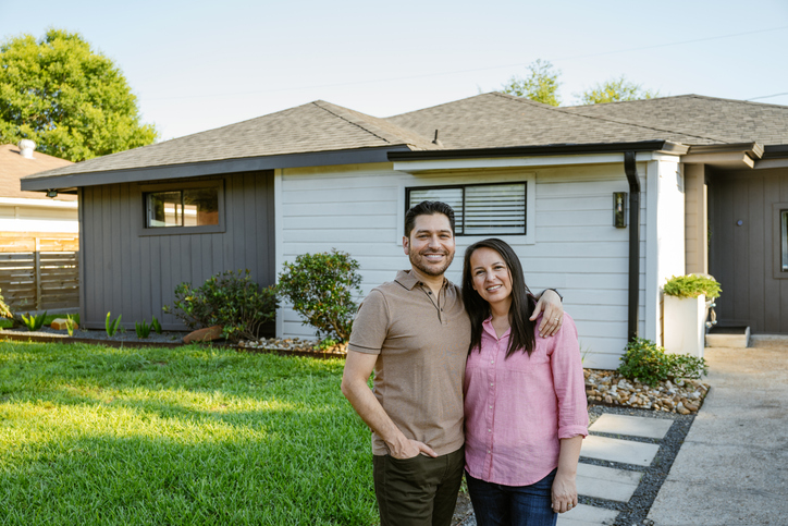 A smiling couple standing together in front of their home