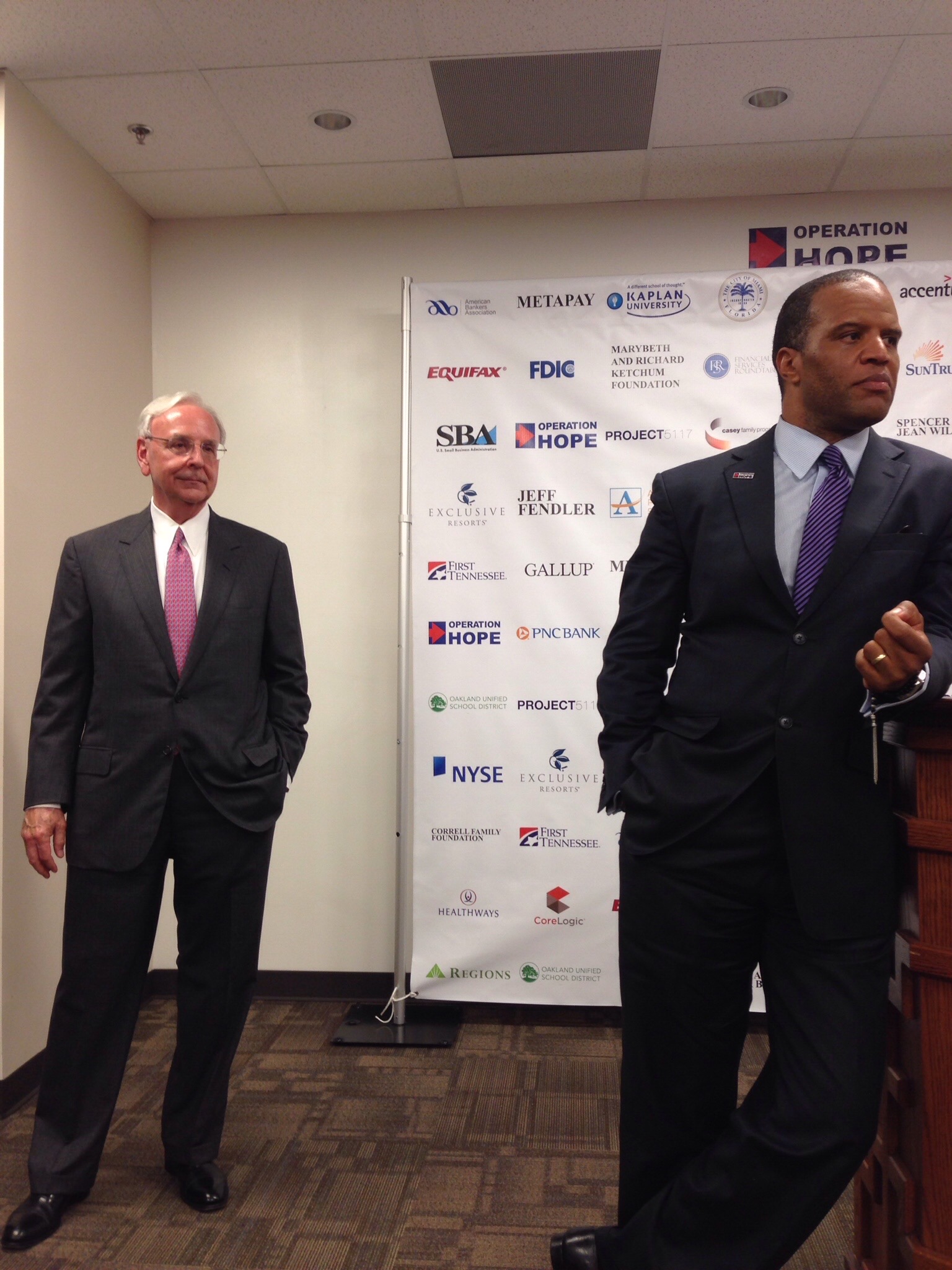 John Hope Bryant and Jim Wells standing in front of an Operation HOPE partner backdrop
